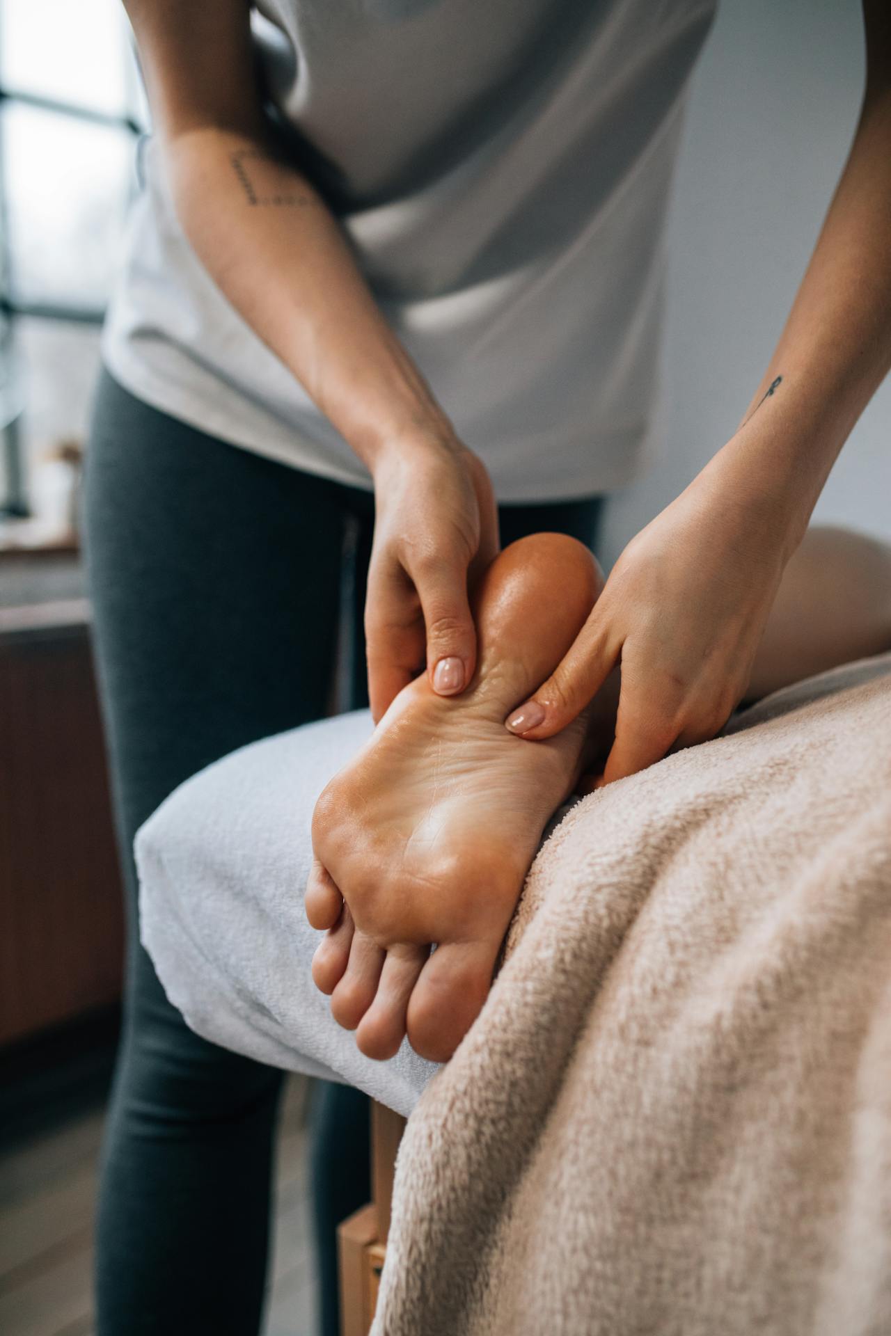 A patient lying on a bed receiving a back foot massage from a podiatrist.